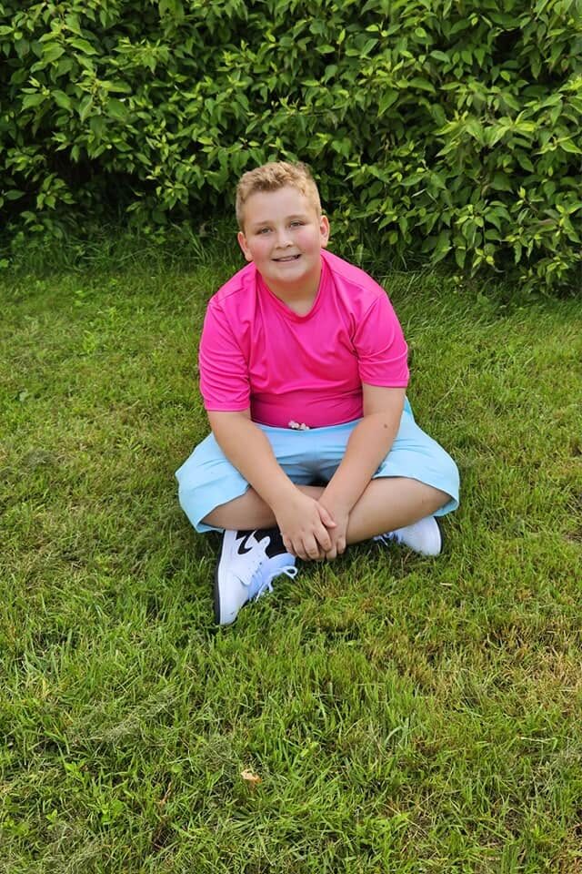Candid outdoor portrait of a boy sitting in the sunlit grass